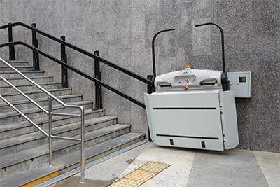 Moderner hochgeklappter plattformlift fur rollstuhlfahrer installiert an einer ausentreppe mit metallgelander an einer grauen betonwand